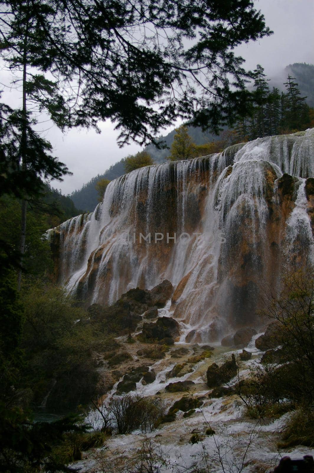 Scenic View of Waterfall Cascading Over Cliff onto Jagged Rocks Below in Forest Setting on Overcast Day in Wilderness China