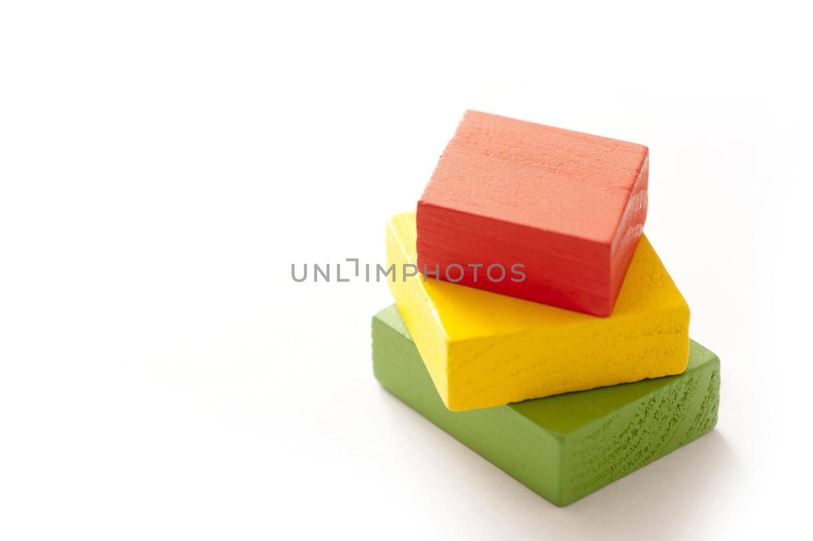 Three educational wooden toy blocks in different sizes and colors - red, green and yellow - stacked on top of one another on a white background with copy space