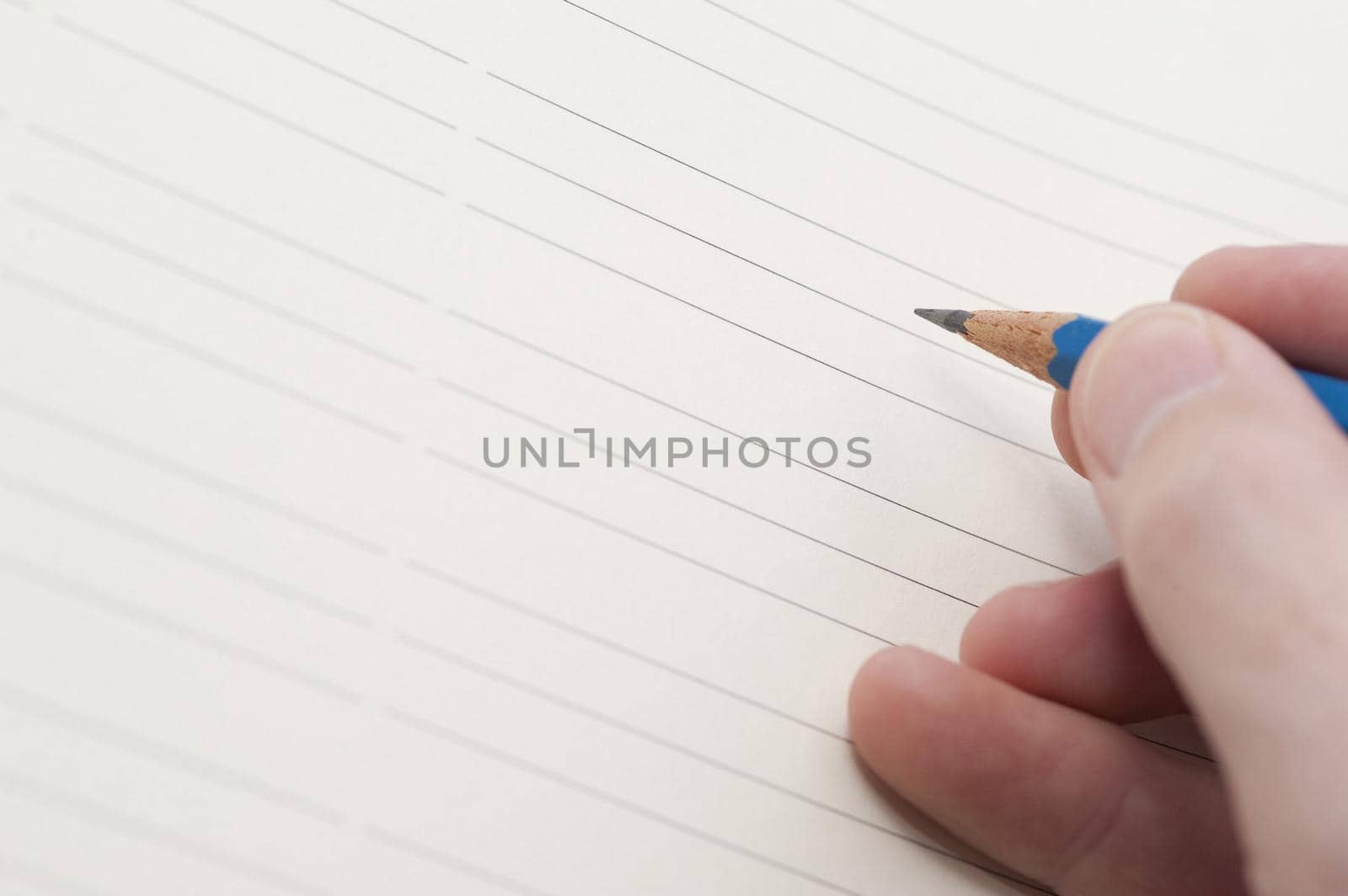 Male hand holding a pencil ready to commence writing on a blank lined sheet of paper