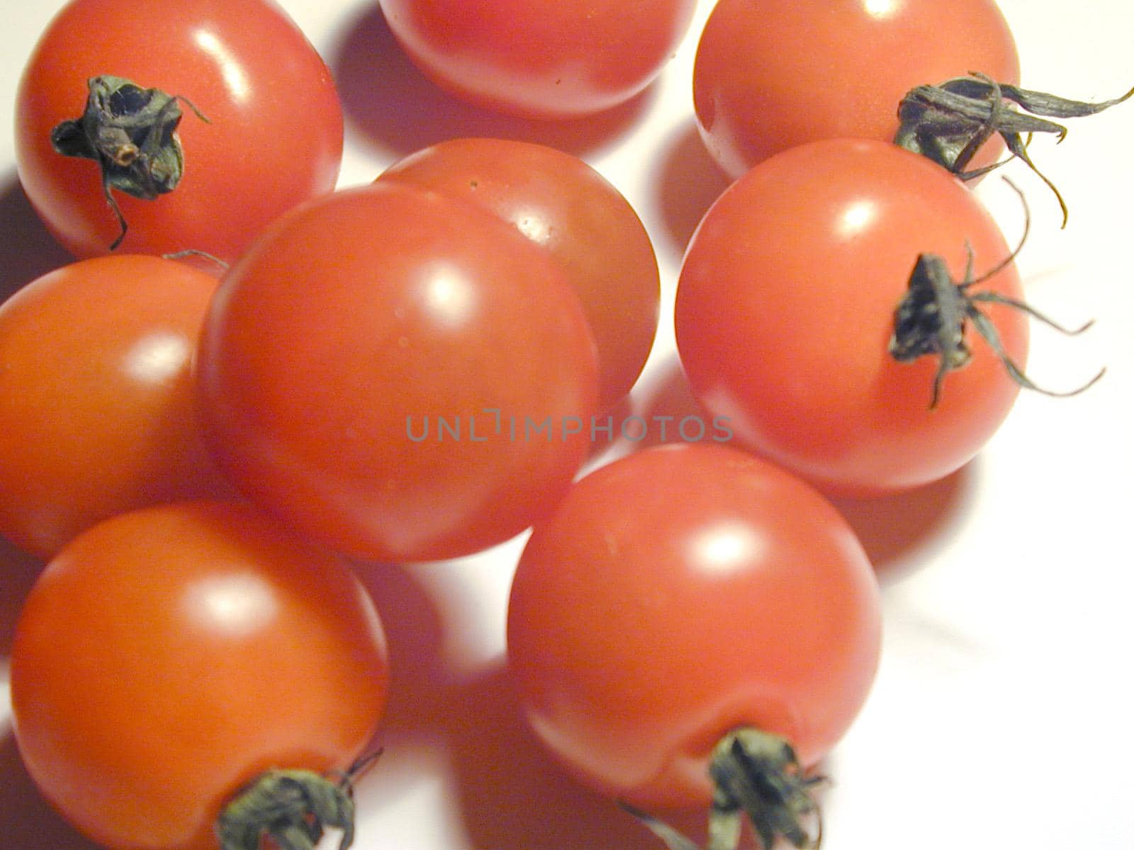 Close up of a pile of fresh ripe red cherry tomatoes with green stalks on a white background for use as a healthy ingredient in salads and cooking