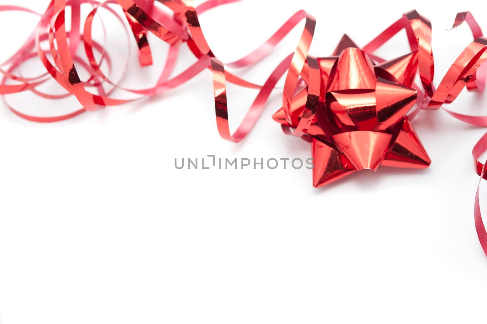 Metallic red foil ornately tied bow and twirled ribbon used to decorate Christmas gifts lying on a white background with copyspace