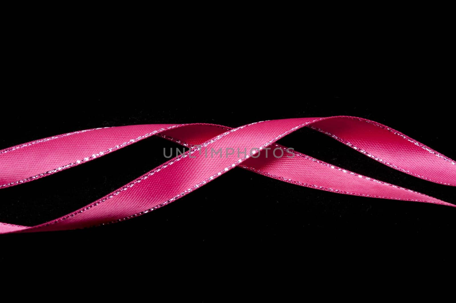 Twirled pink ribbon festive border on a dark background with copy space above and below for your greeting