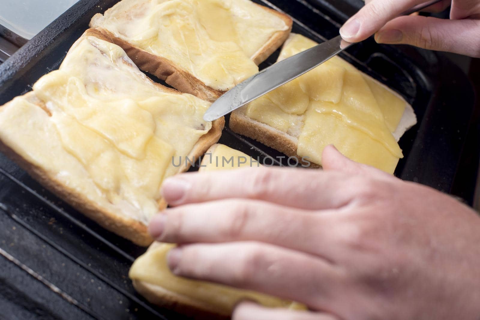 Hands with blunt knife handle toast and cheese melting on four slices of white bread on grill