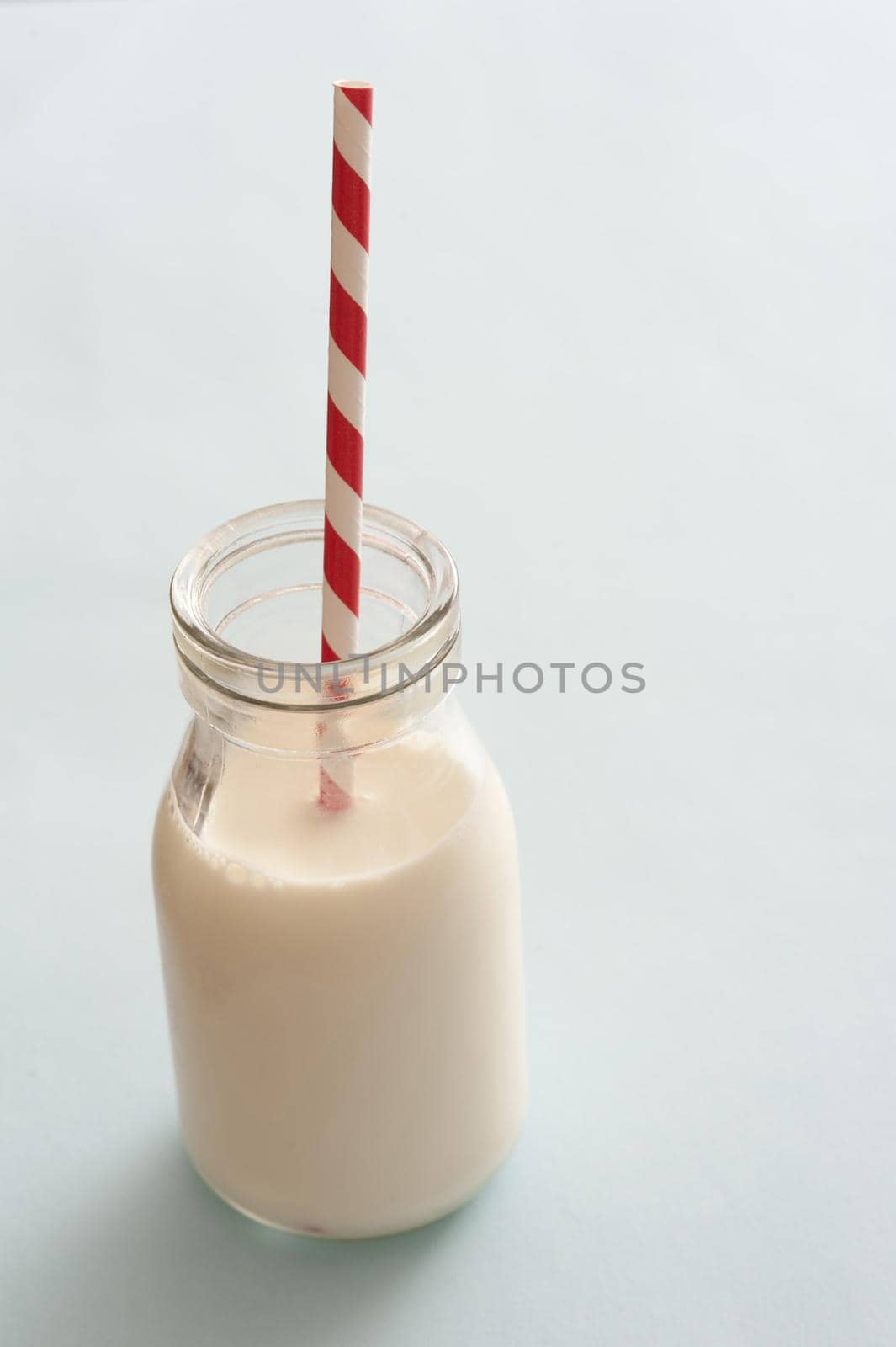 Little jar of milk with red and white straw stuck on top over neutral background with copy space