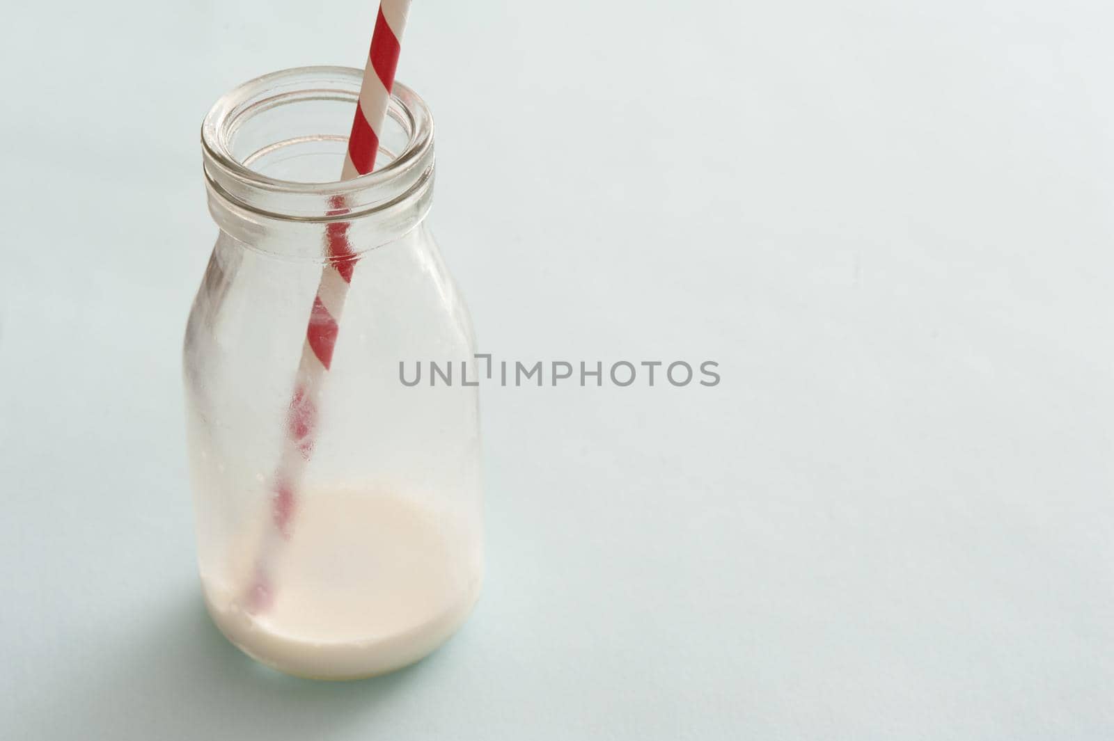 Lone glass bottle nearly emptied of white milk and having a single striped straw