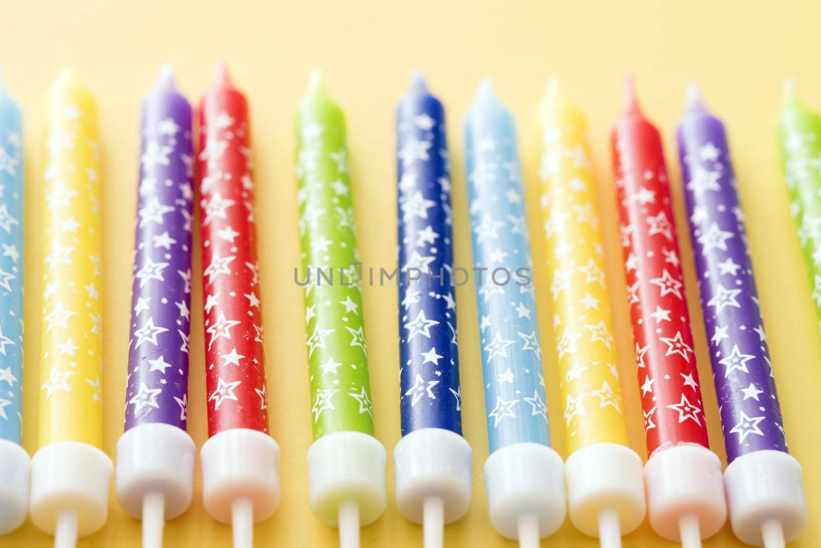 Colorful row of birthday cake candles in the colors of the rainbow decorated with festive stars on a yellow background