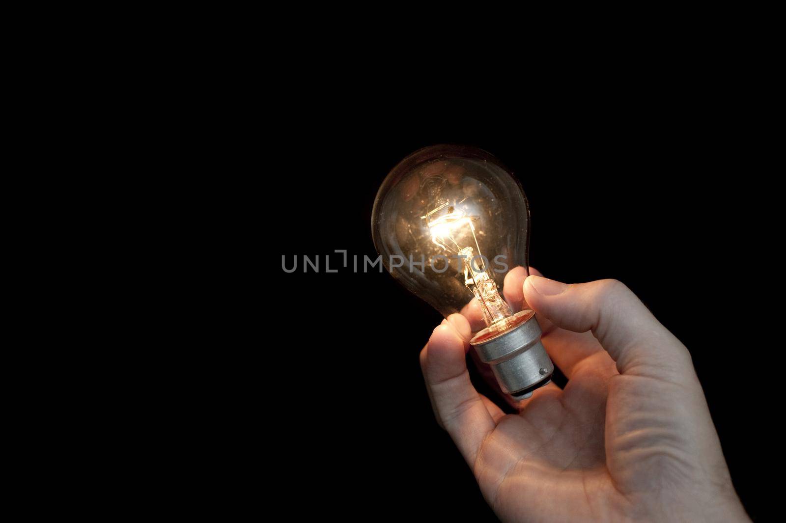 a hand holding a glowing light bulb with a black background