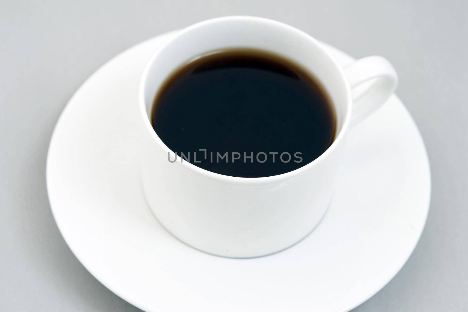 Cup of black espresso on white saucer. Grey background