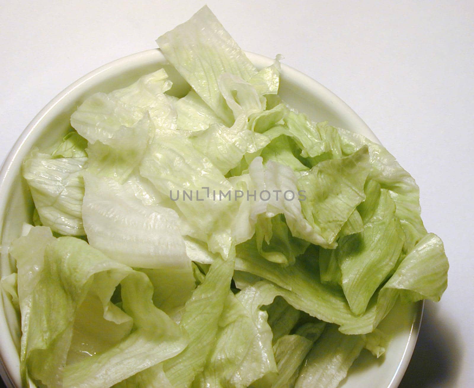 Closeup of a white bowl of shredded iceberg lettuce over white background