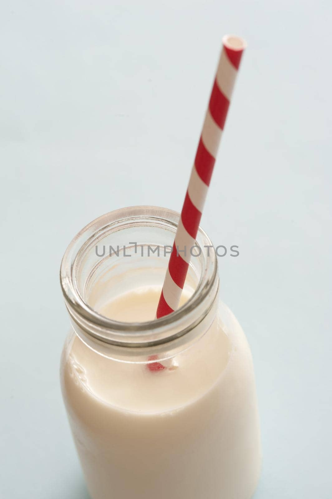 Glass bottle full of milk served with a striped red and white straw over a light grey background with copy space for a healthy drink rich in calcium