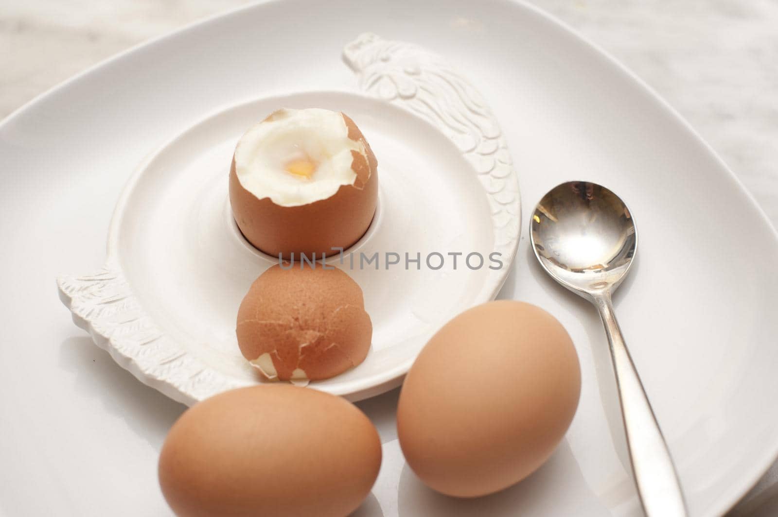Serving of three boiled eggs for breakfast with two eggs on the side and the third soft-boiled egg with its top cut off in an eggcup
