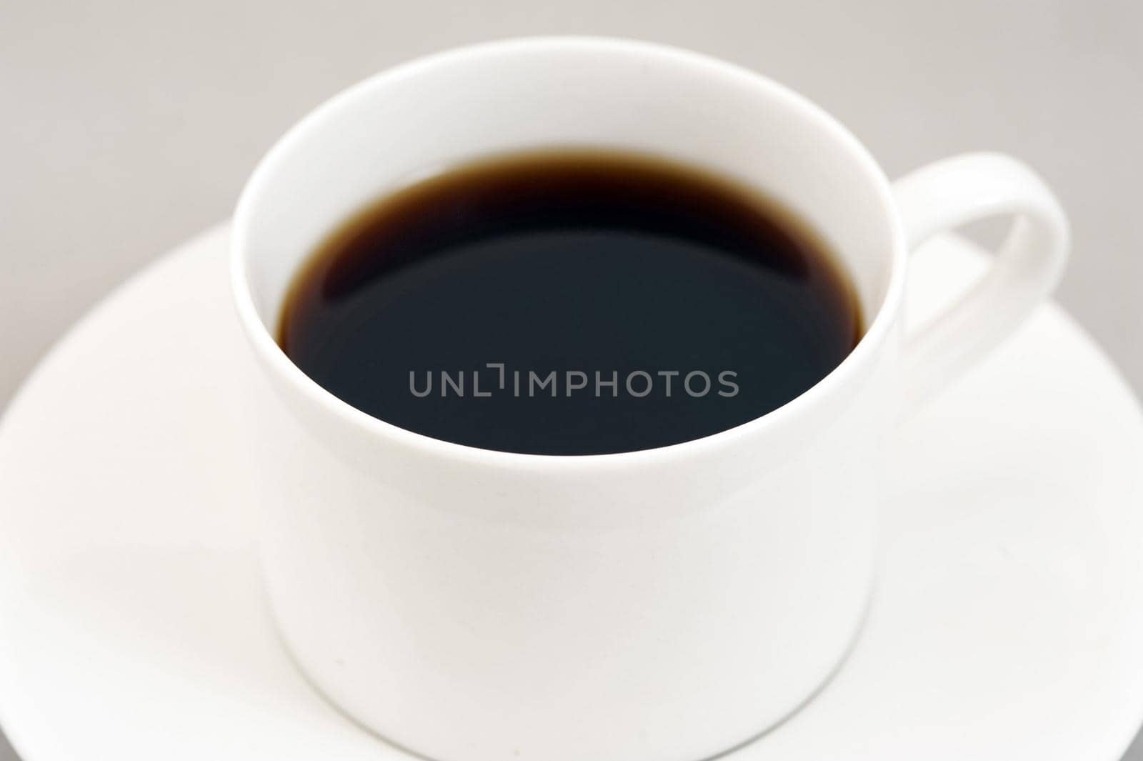 Black energizing coffee served in a white round cup on a saucer made of porcelain, close-up