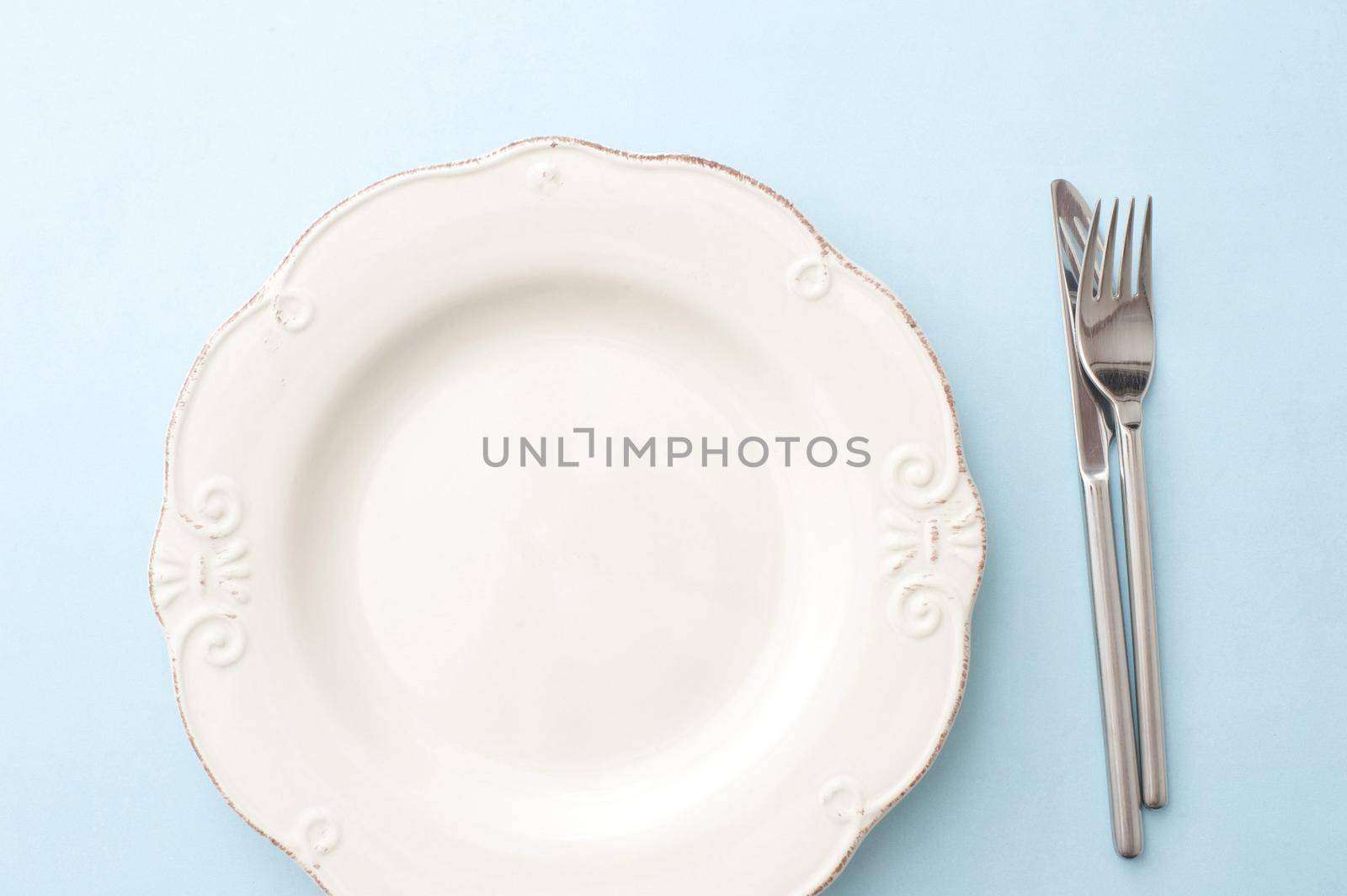 Clean empty white dinner plate on a table with cutlery alongside viewed from overhead in a food and catering concept
