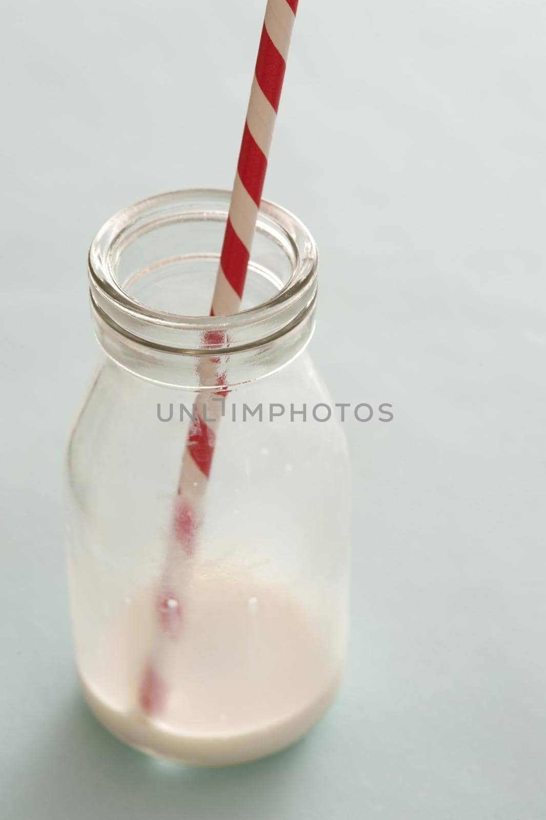 Small empty milk bottle with a colorful red striped straw and the remnants of the consumed drink in the bottom, close up high angle conceptual of a healthy diet for kids
