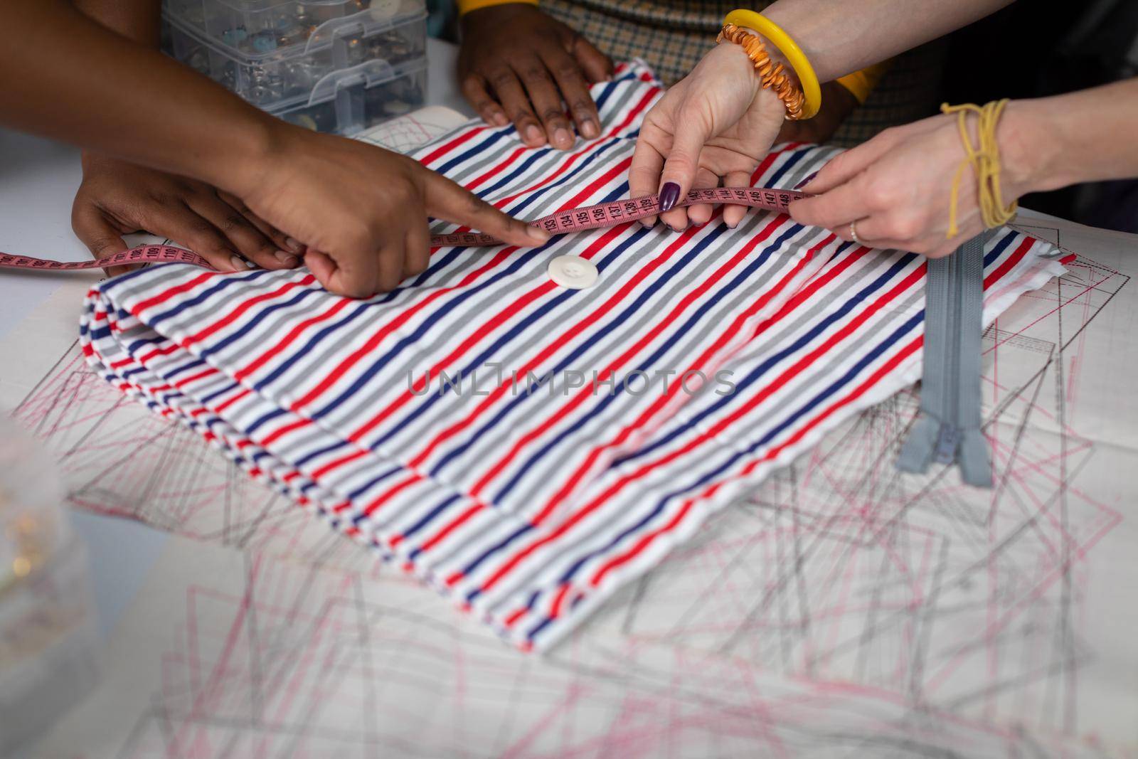 Matching the button to the fabric. Index finger. Hand of a dark-skinned woman and a European woman. The background of a tailor's workshop.