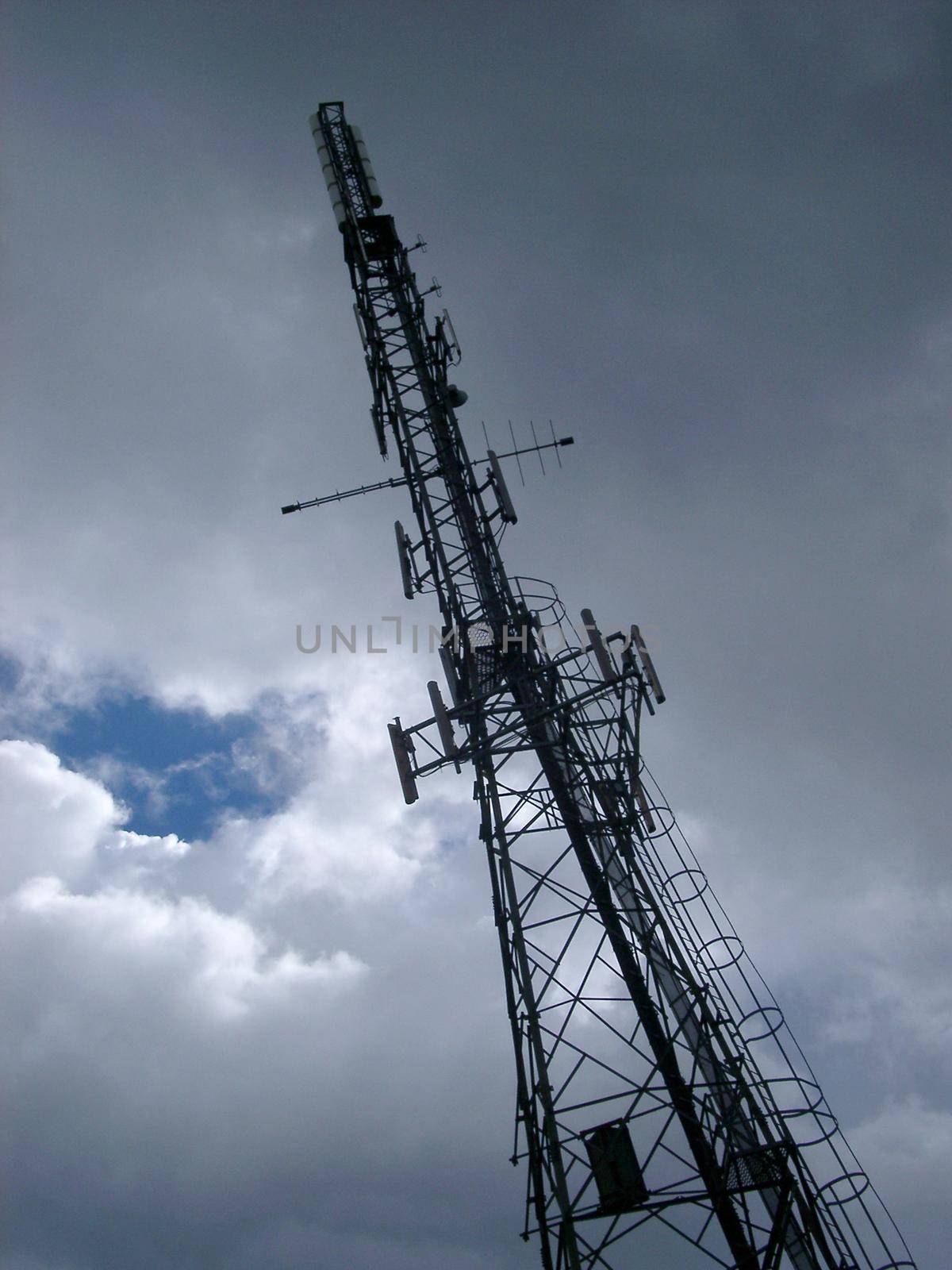 Vert tall steel lattice communications tower stretching up towards the cloudy blue sky with antennas and radio dishes mounted up its length
