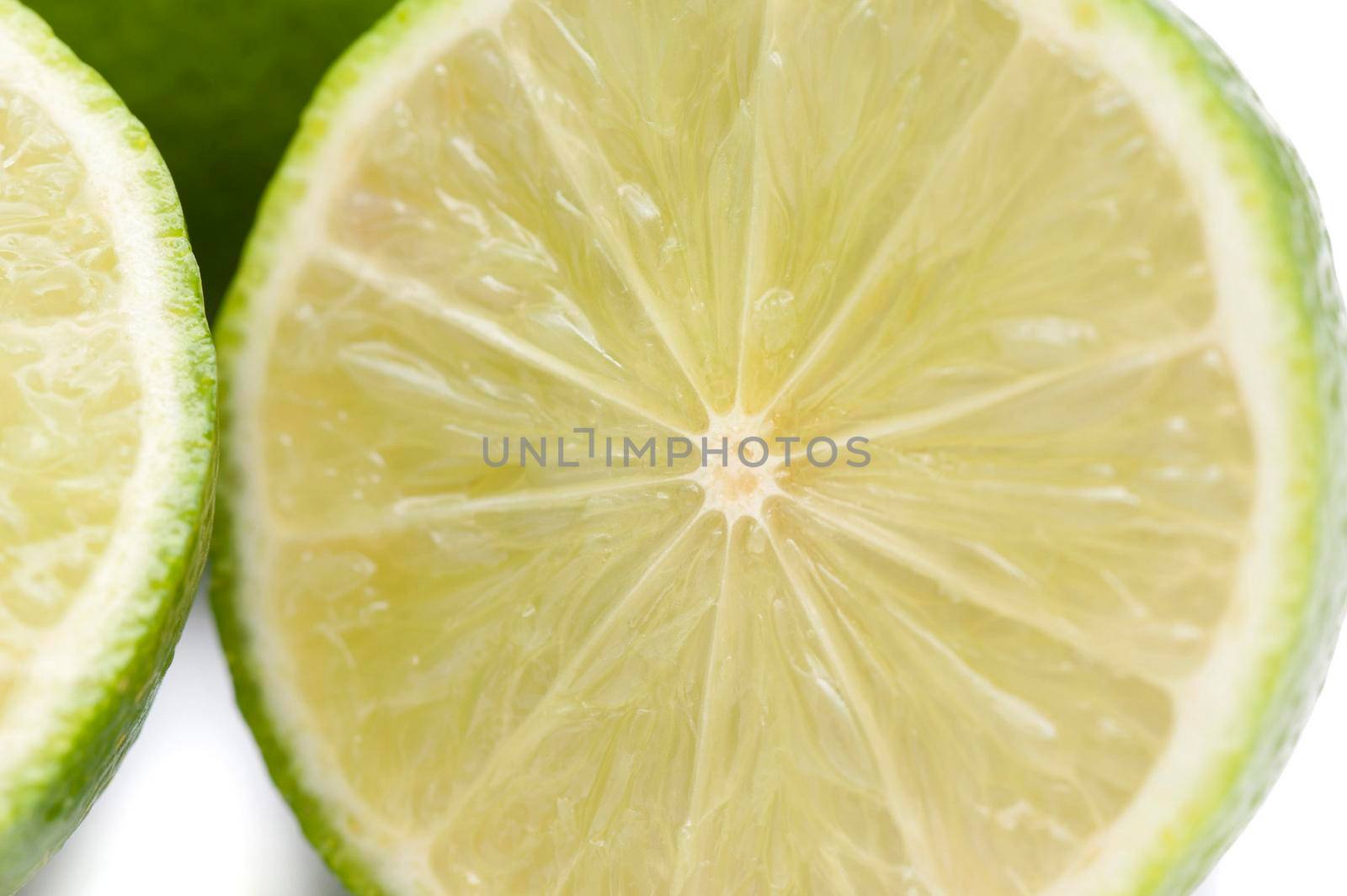 Halved lime detail showing the texture of the juicy pulp, rind and segments over a white background