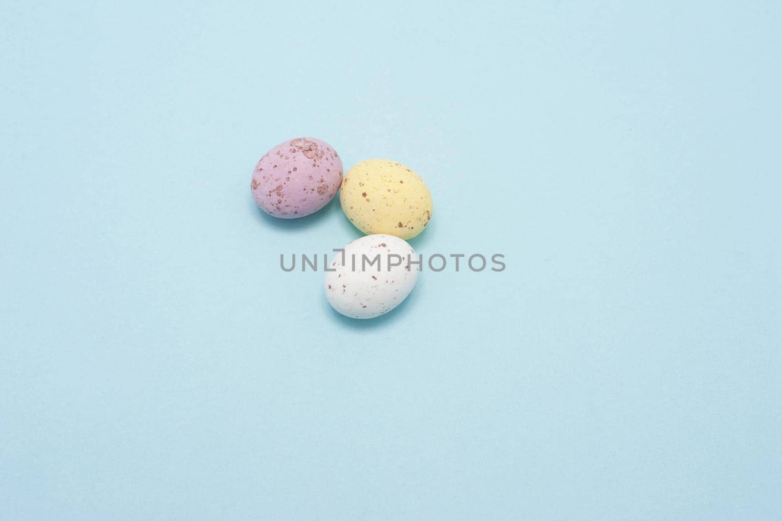 Three small sugared chocolate Mini Eggs on a blue background with plenty of copyspace for Easter