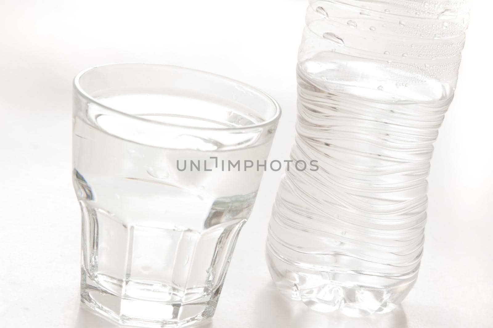 Glass of pure bottled water in a glass tumbler with a plastic water bottle behind, over white