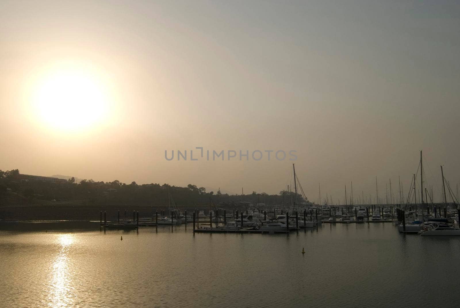The sun makes a valiant effort to shine through thick hazy smog caused by air pollution over a coastal marina with small boats and pleasure yachts moored at the jetties