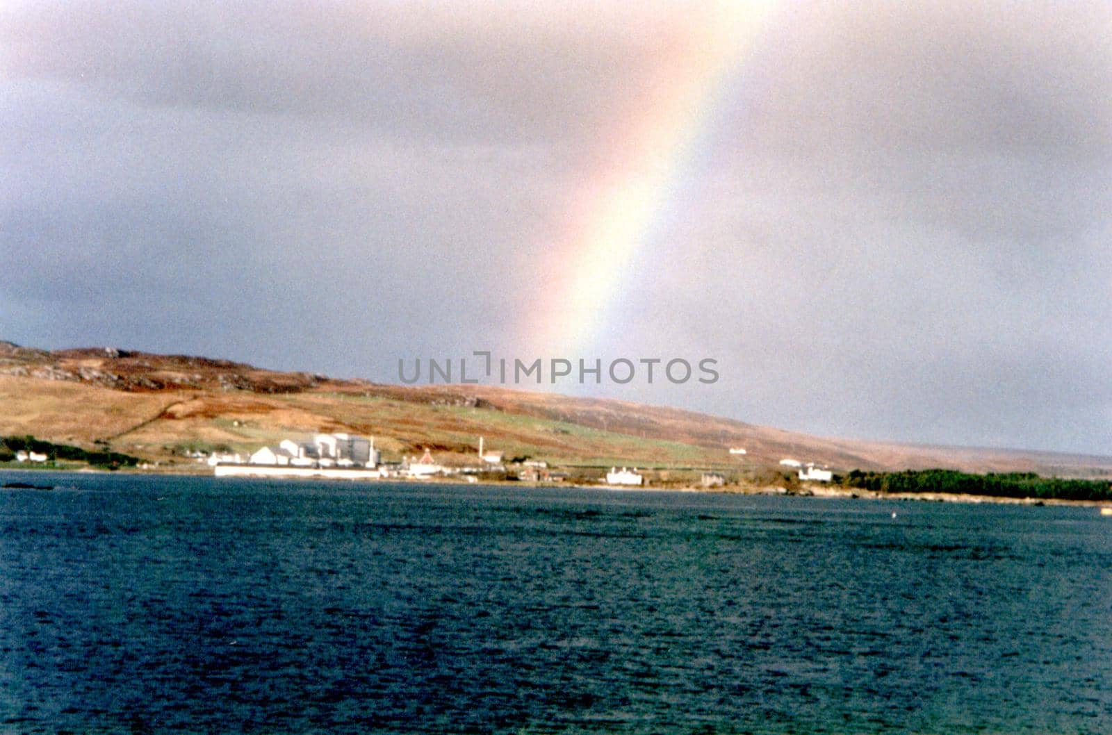 Colorful rainbow in stormy grey cloudy coastal skies above a small fishing village in a bay viewed across the water