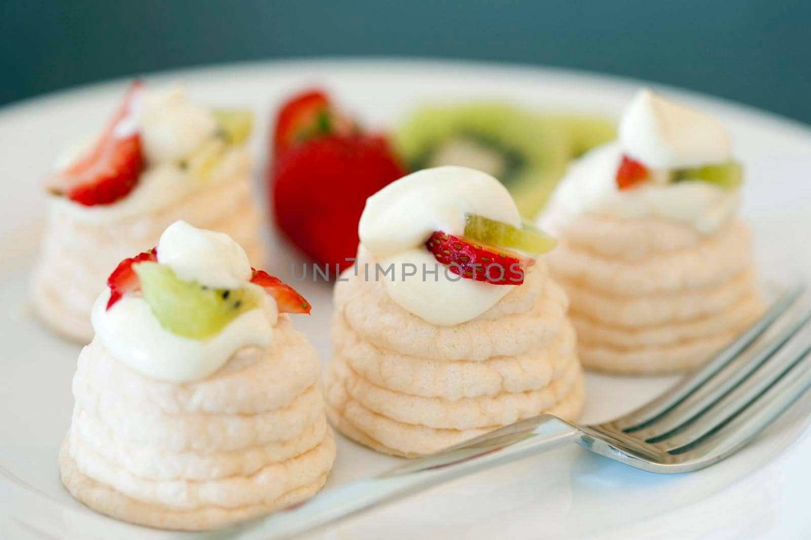 Indiviual meringue pavlovas with decorative twirled cases filled with whipped cream, strawberries and kiwi fruit