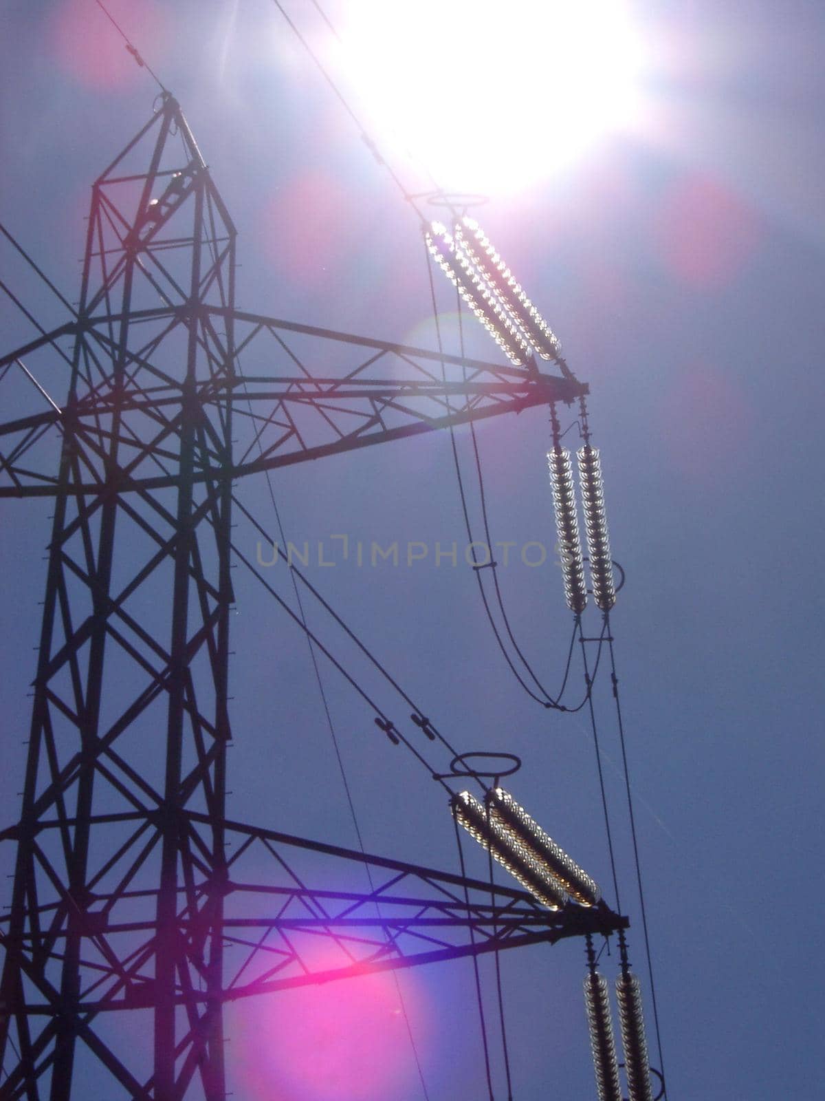 View looking up into the sun of a high voltage electricity pylon with pink sun flare spots