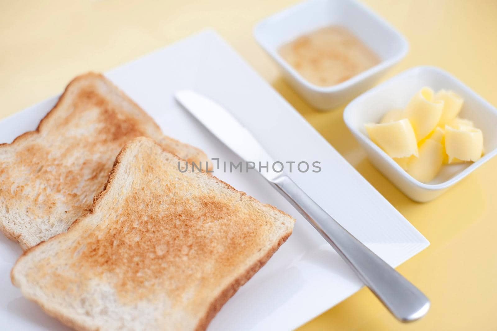 White toast on a plate served for breakfast with individual dishes of rolled butter and marmalade, high angle view
