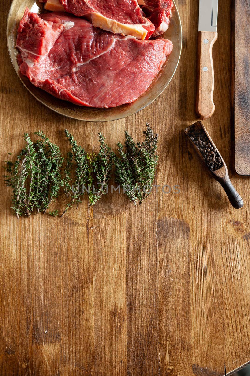 Top view of raw fresh meat next to green rosemary , pepper beans and chef knife. Kitchen table.