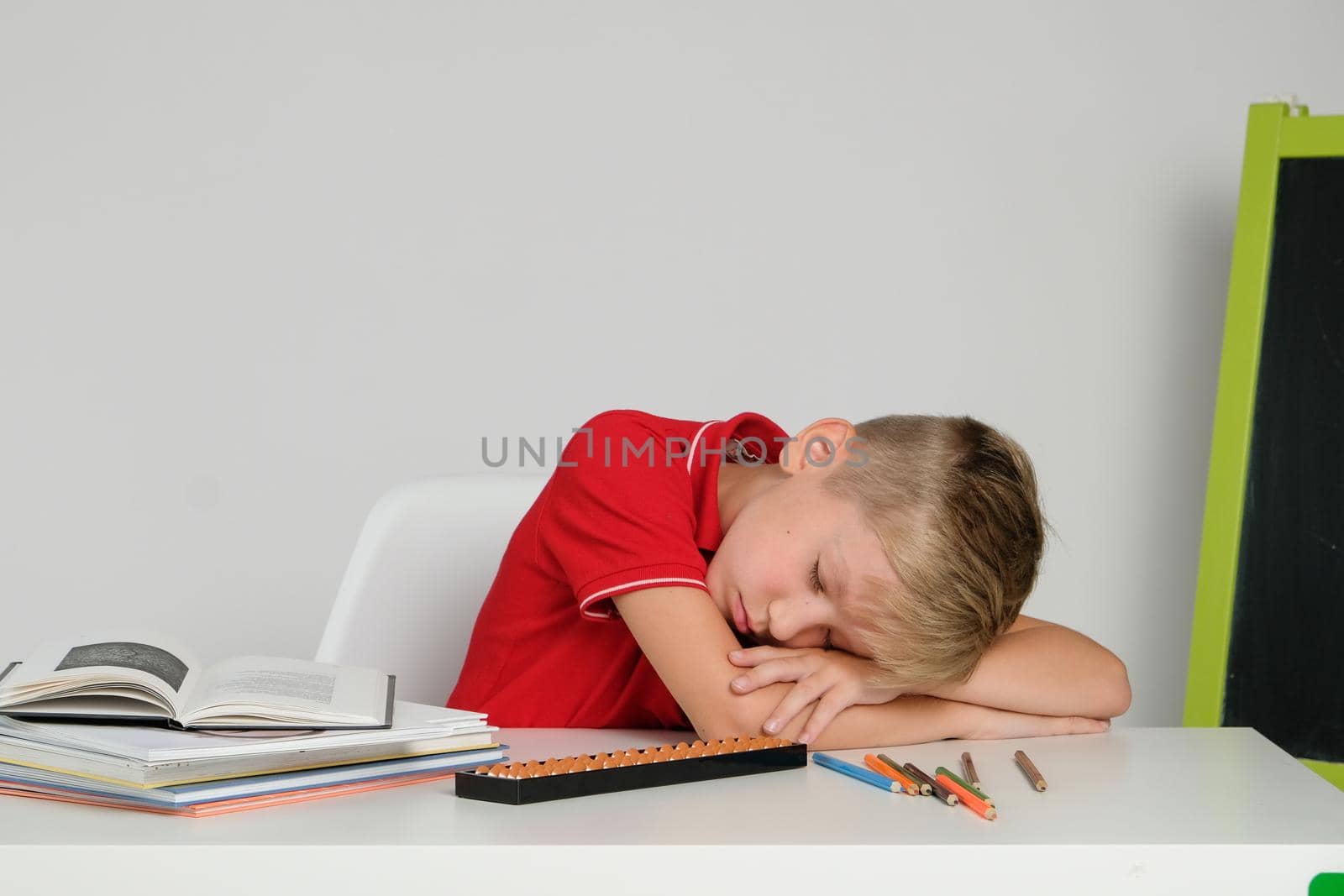 Little boy feeling tired bored and sleepy doing school homework at the table. by natus111