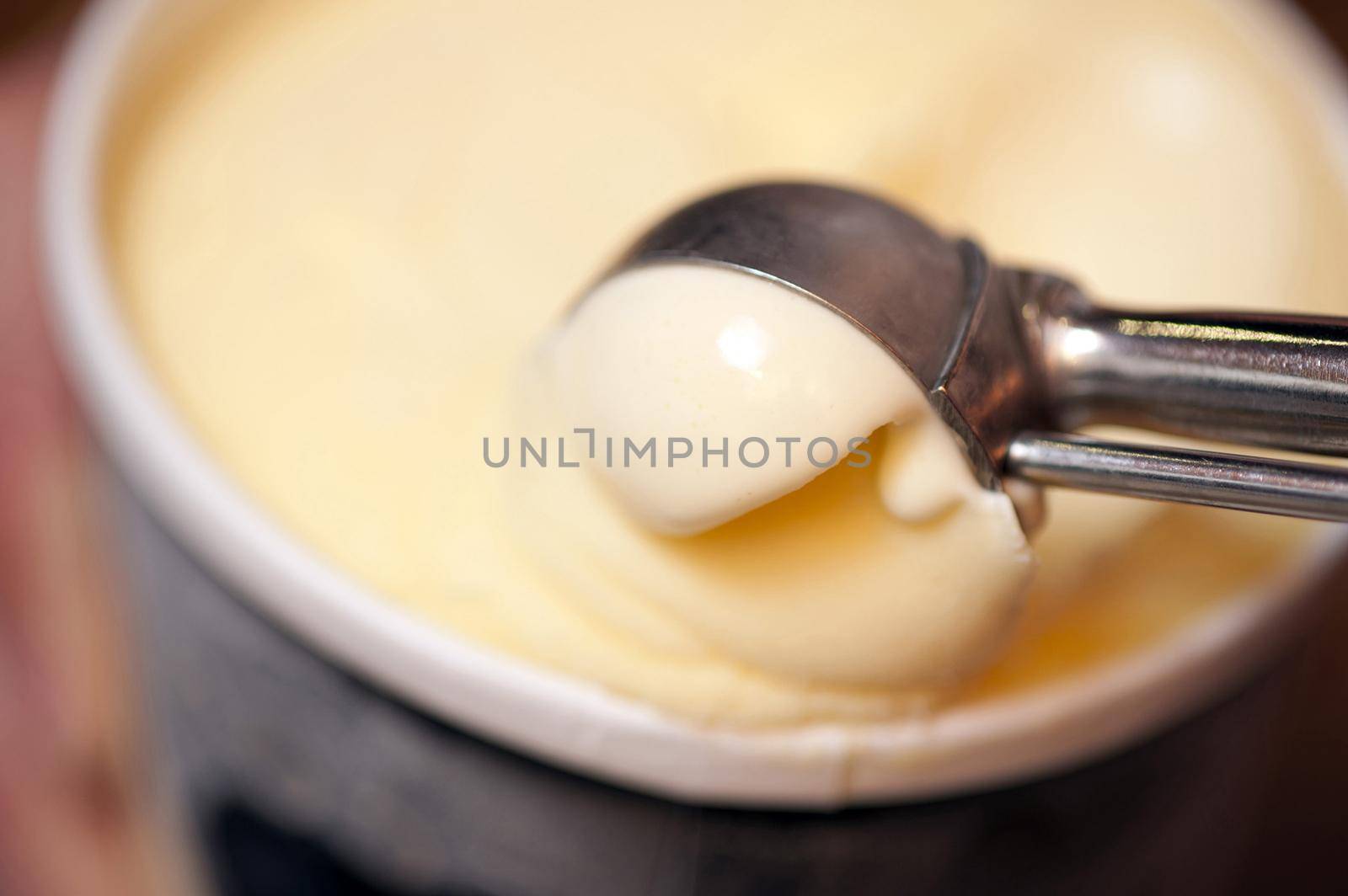 Serving a scoop of rich creamy vanilla ice cream from a small bowl with a stainless steel kitchen scoop, close up soft focus