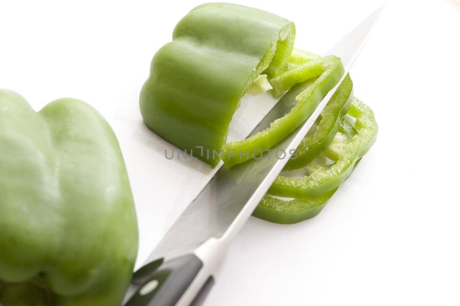 Close-up of green pepper cut in slices with knife. White background