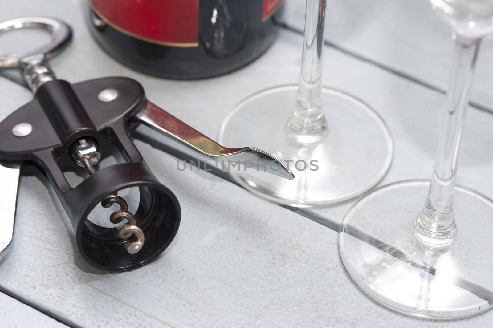 Lever style corkscrew bottle opener alongside wineglasses and a bottle of wine on a white wooden table