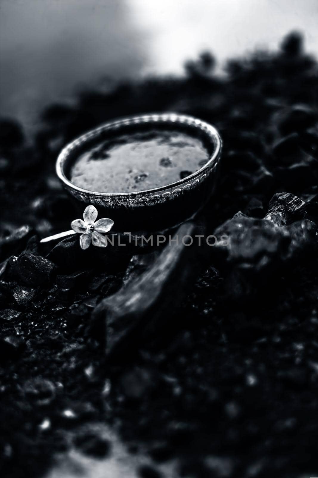 Close up of activated charcoal in a glass bowl on the wooden surface along with some raw powder of charcoal or coal spread on the surface. by mirzamlk