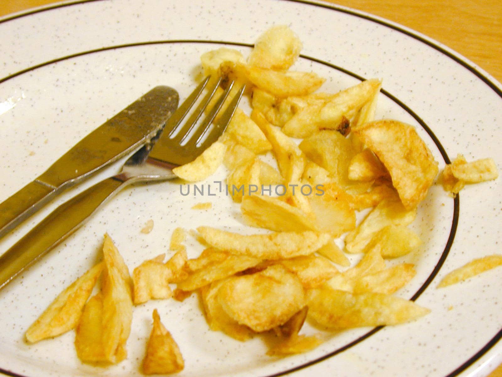 Half eaten plate of golden deep fried potato chips on a plate with cutlery in a chip shop