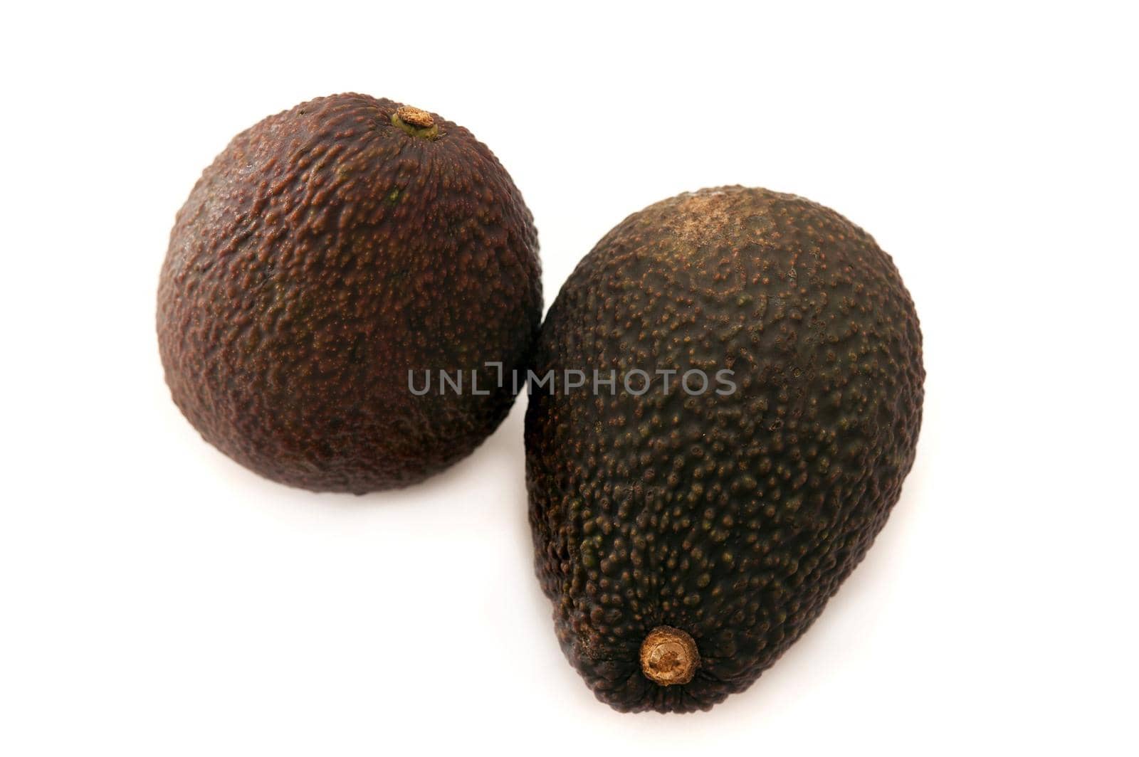 Two whole fresh ripe avocado pears, Persea americana, with one viewed on its side and the other from the top over white