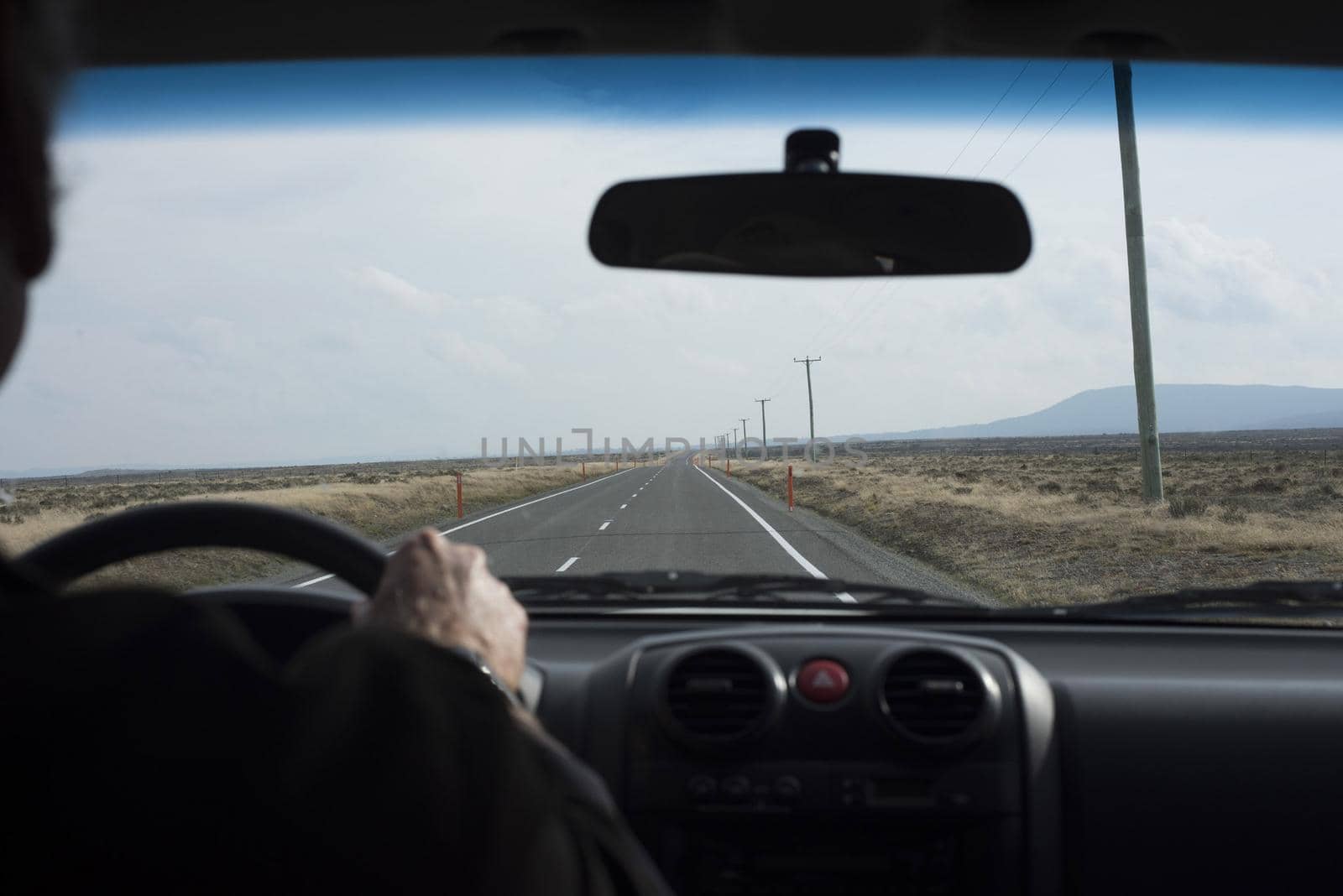 Long journey ahead concept with man driving a car in an over the shoulder perspective looking at the long road stretching into the distance through the windscreen