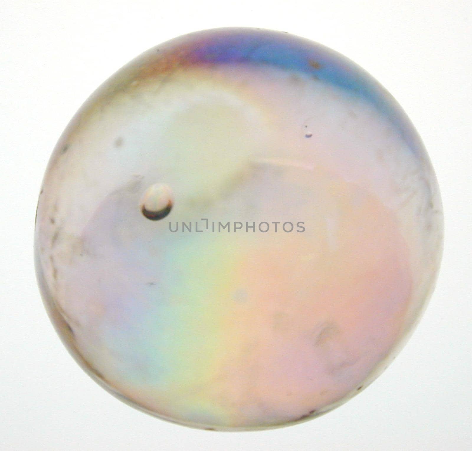 Iridescent toy glass marble viewed close up showing the colorful internal refraction of light over white