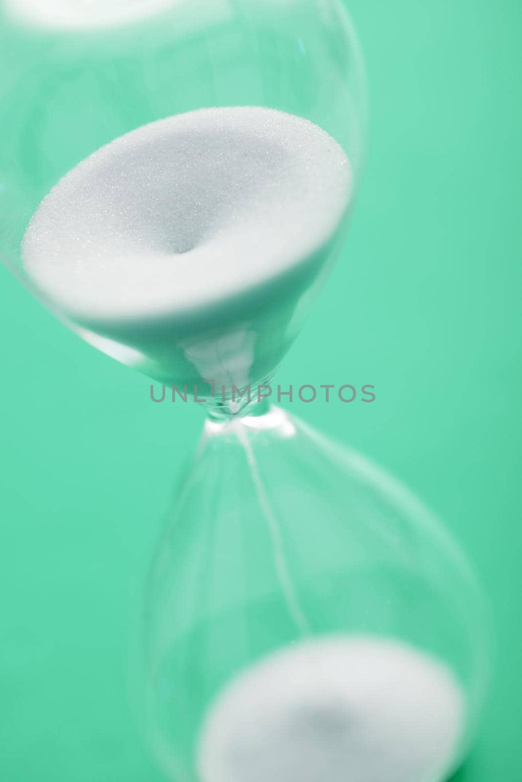 Close up view of hour glass with white sands pouring into lower part against a green background