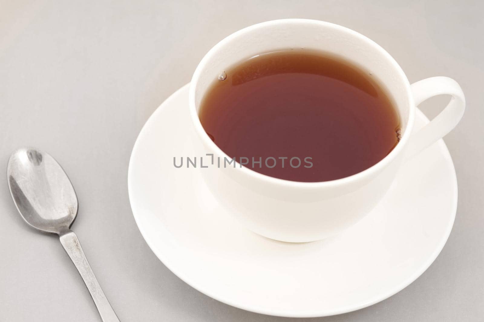 Cup of freshly brewed black tea in a generic white ceramic cup and saucer with a teaspoon alongside, high angle view