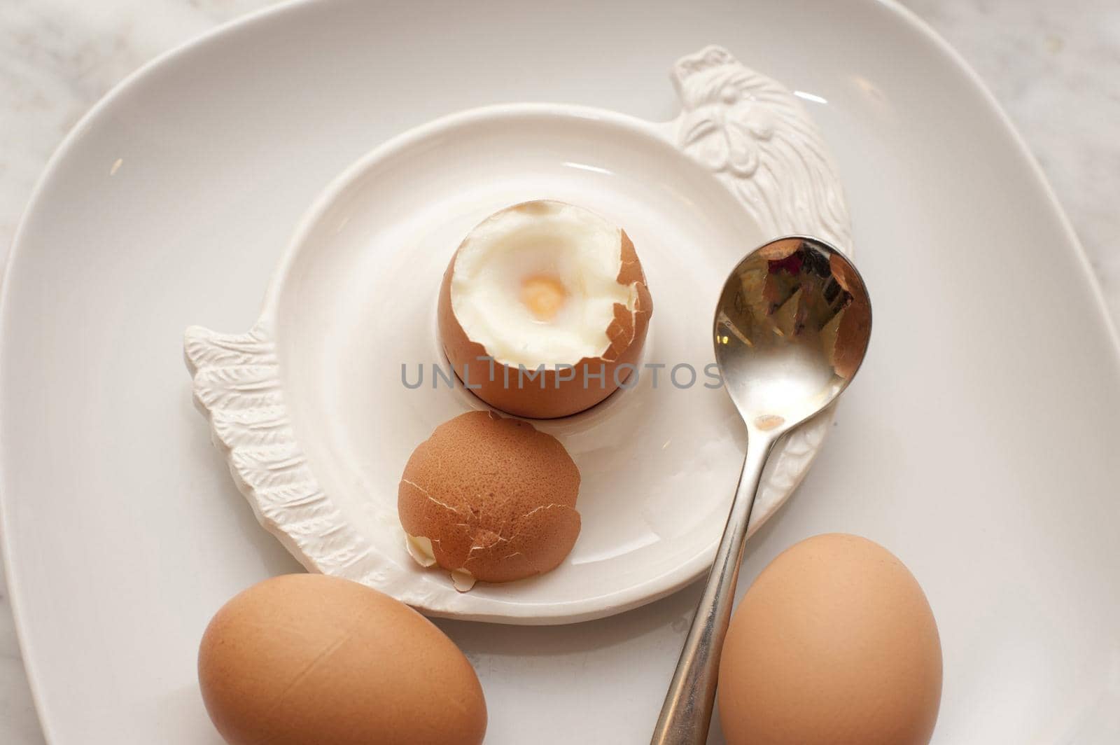 Three boiled eggs for breakfast with one with the top removed ready to eat in an eggcup and the other two lying alongside on the plate