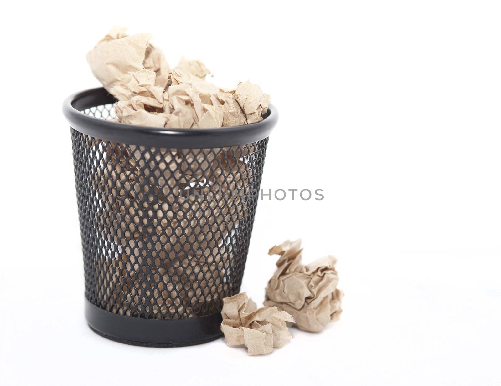 Crumpled waste paper in a bin which is full and overflowing on to the floor