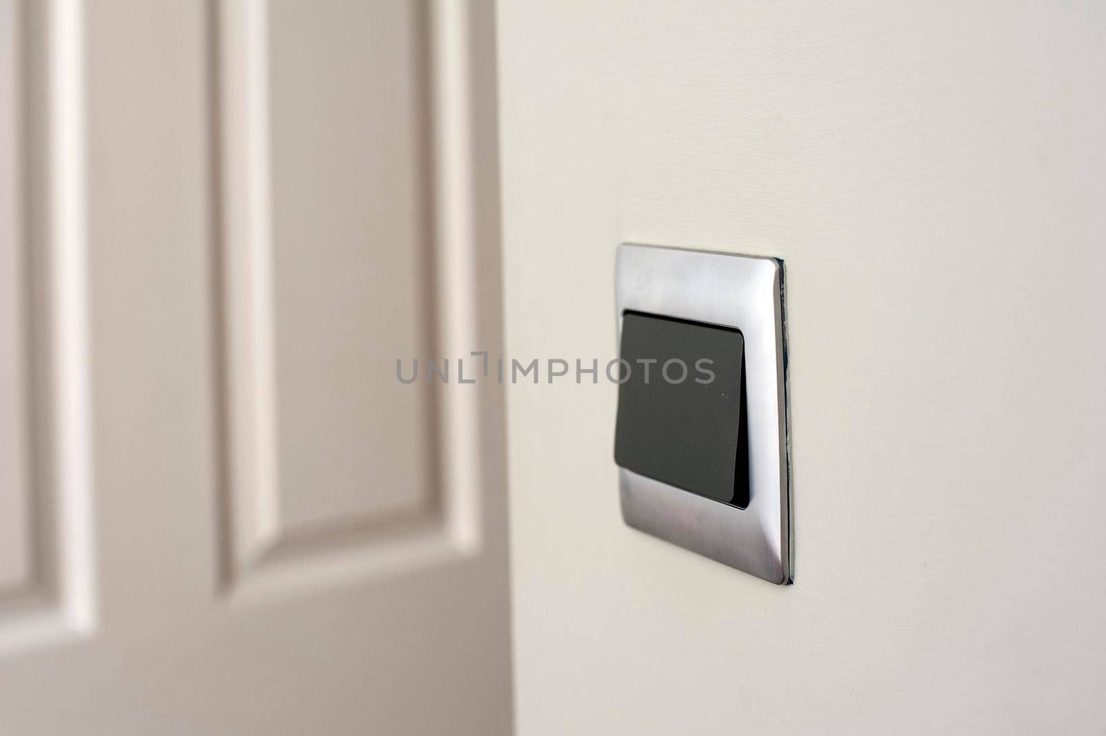 Modern silver framed plastic light switch on a white wall alongside a white painted wooden paneled door