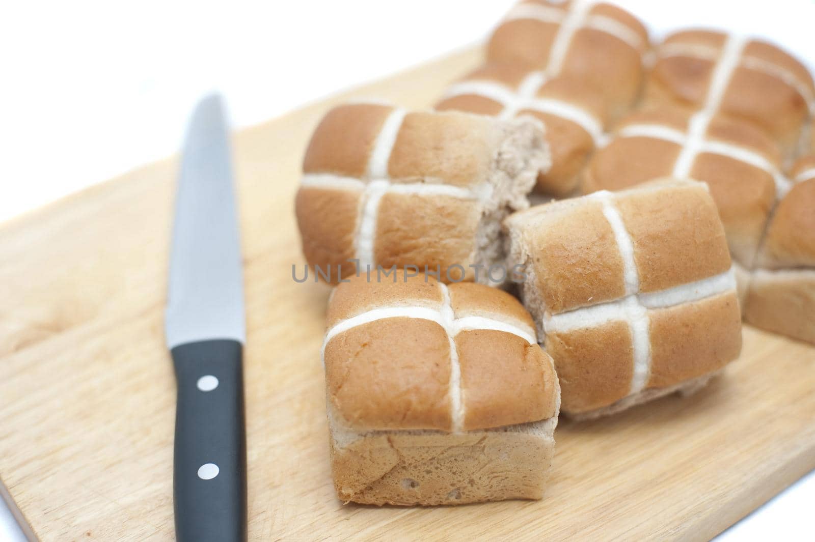 Fresh batch of Easter Hot Cross Buns on a wooden board with a knife