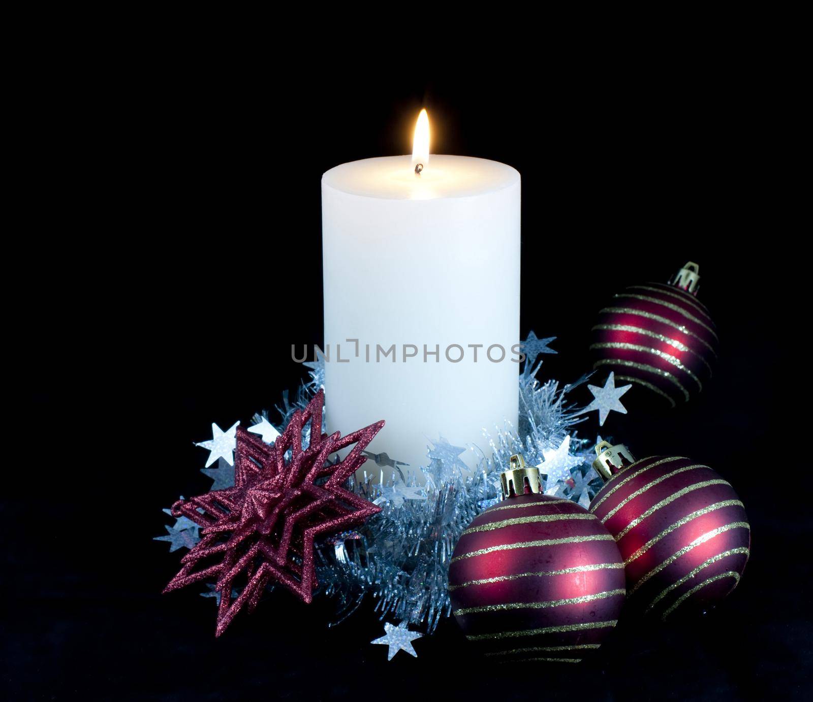 a white candle decorated with christmas balls and tinsel