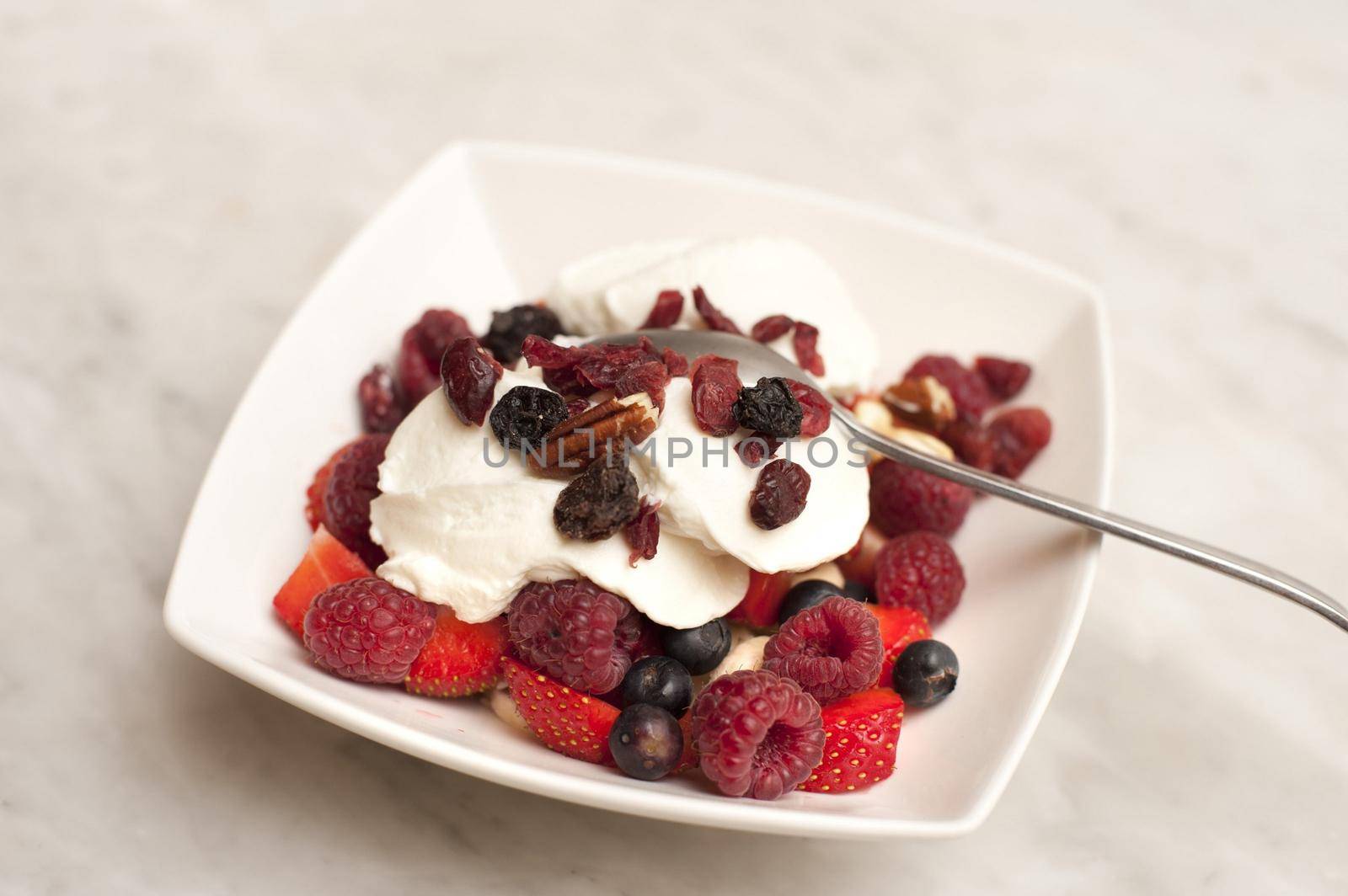 Healthy fruit breakfast with a bowl of raisins, strawberries, raspberries and blueberries served with thick creamy yoghurt