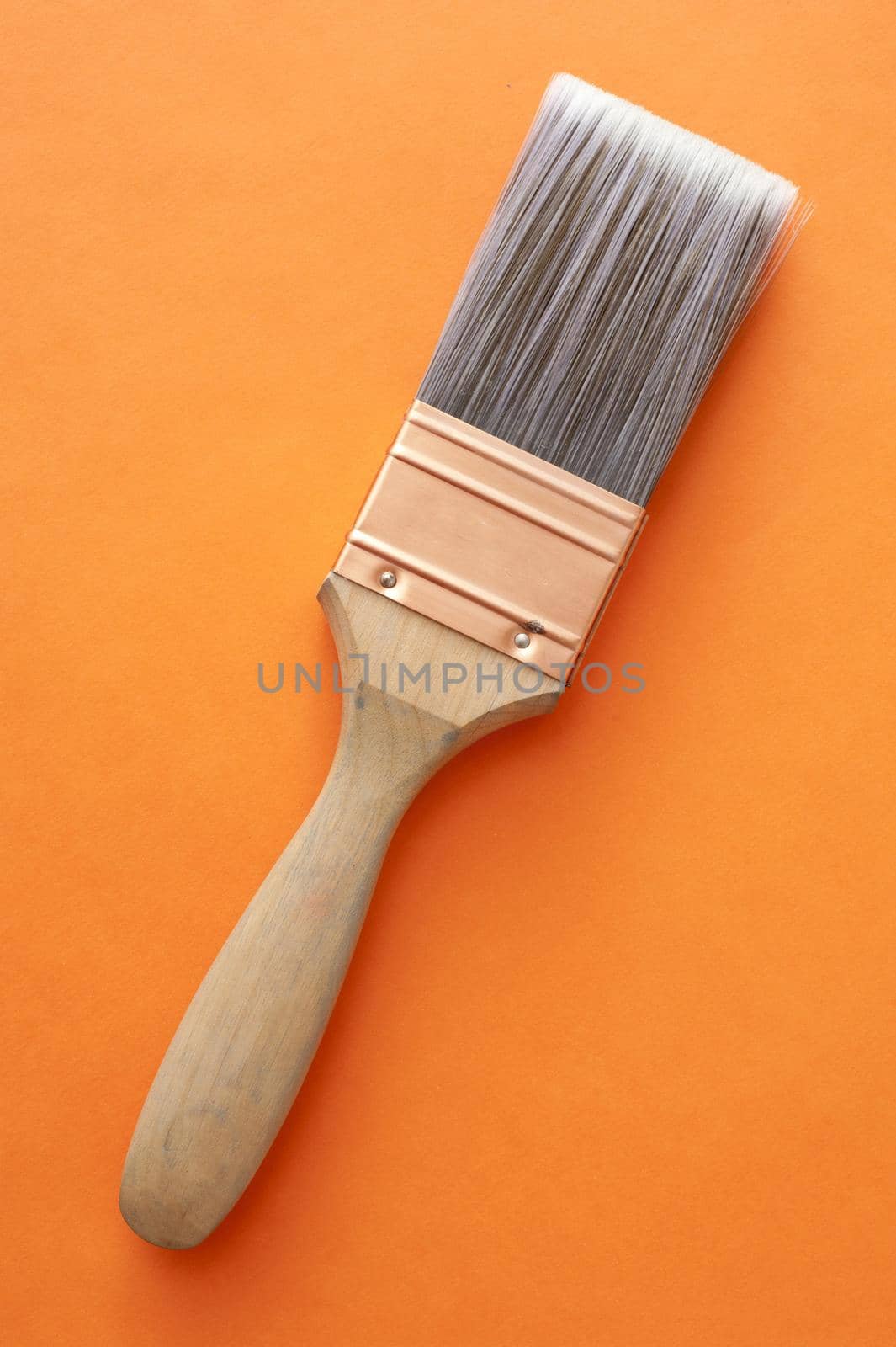 Single large wooden and copper paintbrush placed over orange background at an angle