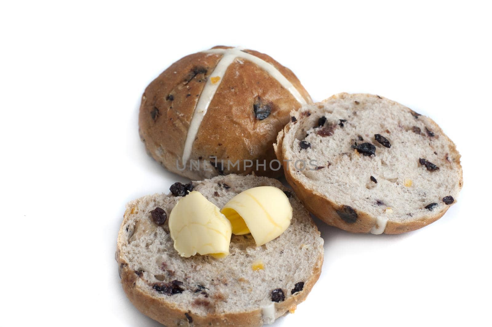 Sliced and buttered spicy fruity Hot Cross bun for Easter with a whole one behind showing the symbolic pastry cross over a white background