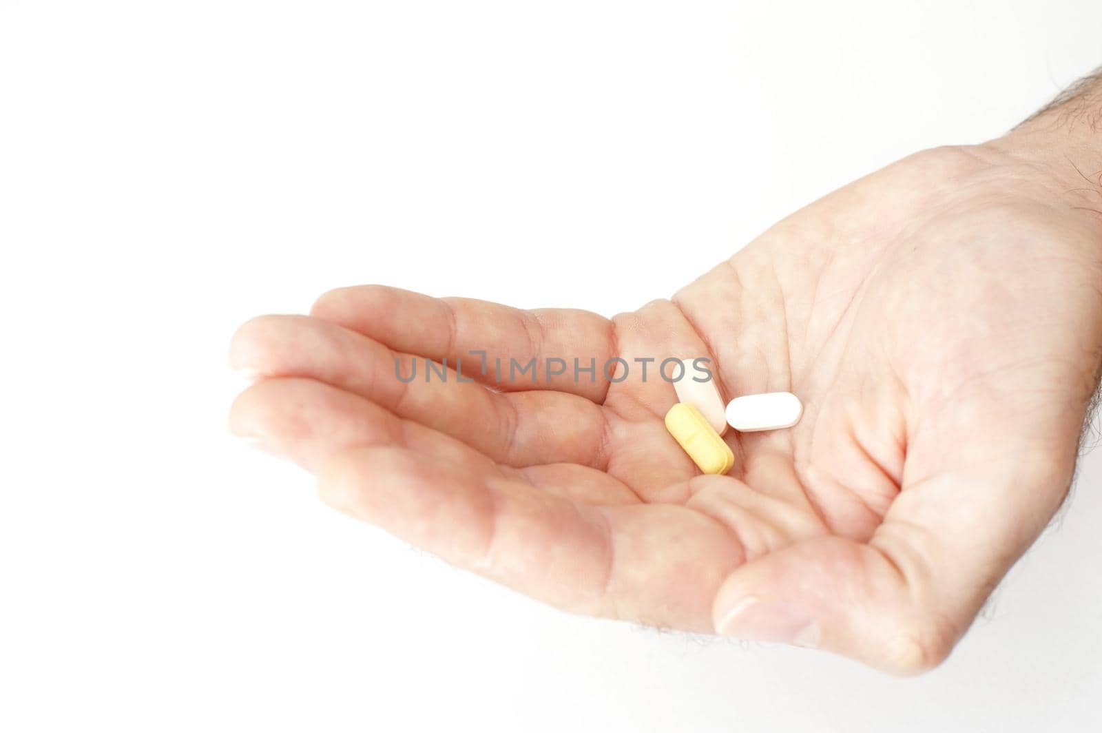 Man holding out his medication in his cupped hand with three different tablets displayed, isolated on white