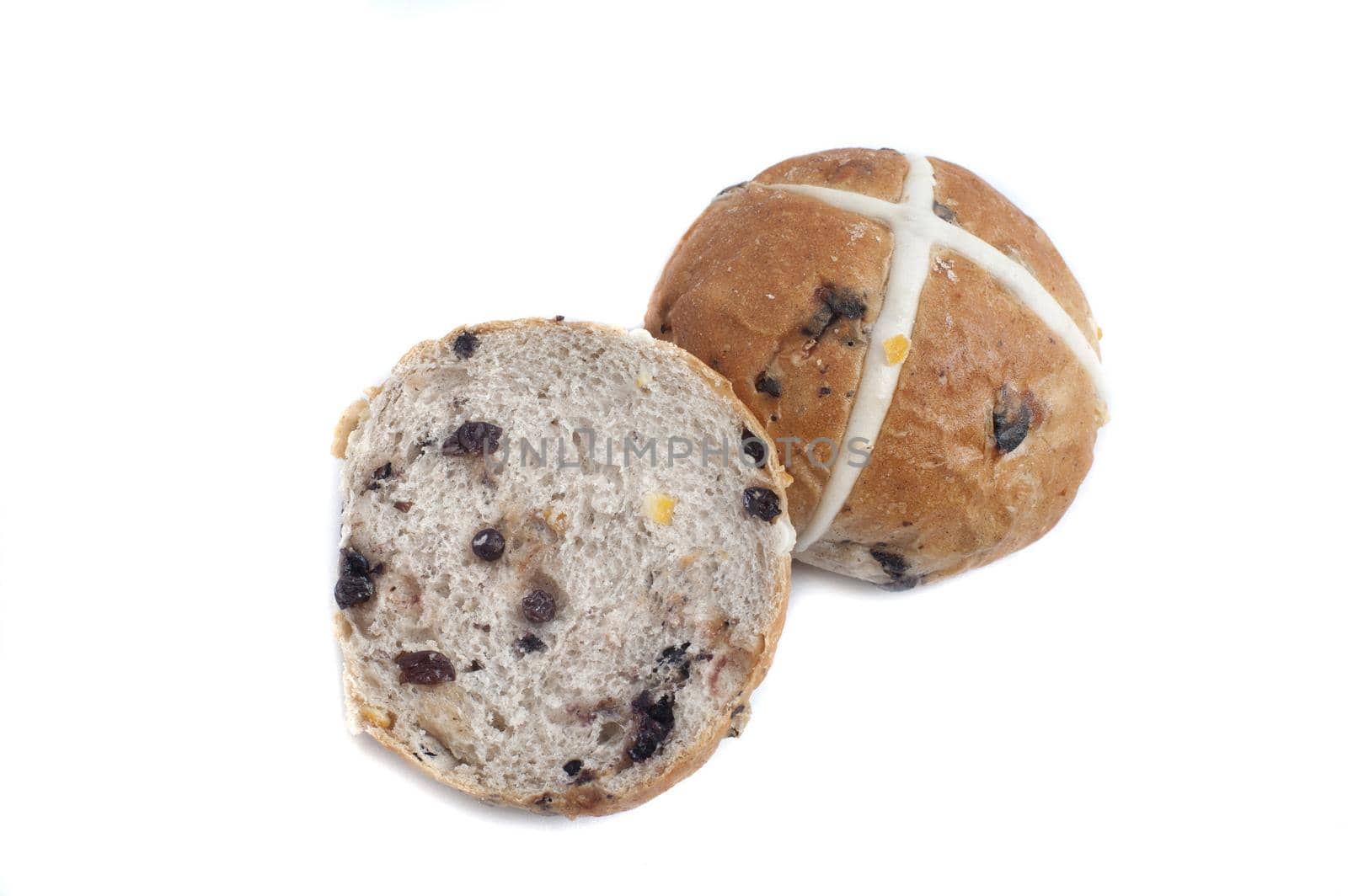 Close up view of sliced hot cross bun with raisins, and one whole bun marked with white cross, isolated on white background